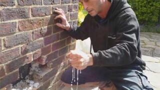 Man controleert spouw op vocht door een gat in de muur te maken